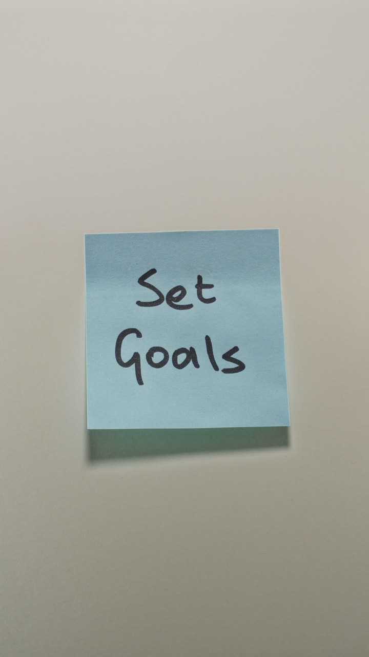 Hands posting Set Goals sticky note on light wall, demonstrating goal setting