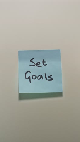 hands posting set goals sticky note on light wall, demonstrating goal setting