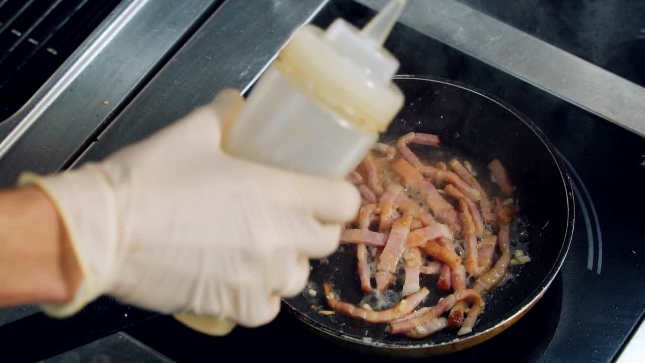 Pouring into frying bacon. Cooking tasty meat on a frying pan. Chef is cooking appetizing bacon adding special ingredients