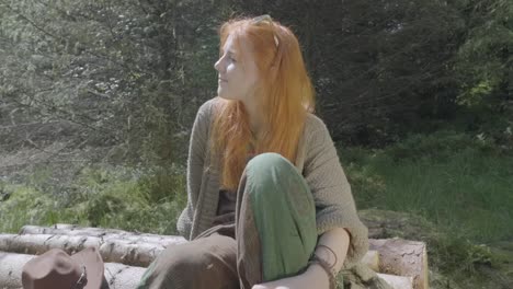 Girl-sat-alone-on-log-pile-in-sunshine-in-forest-in-summer-with-buzzing-insects-at-half-speed-slow-motion