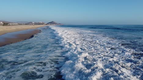 Close-up-flyover-of-blue-water-waves-breaking-at-sandy-beach-during-sunset