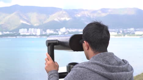 man looking through binoculars at a coastal scene