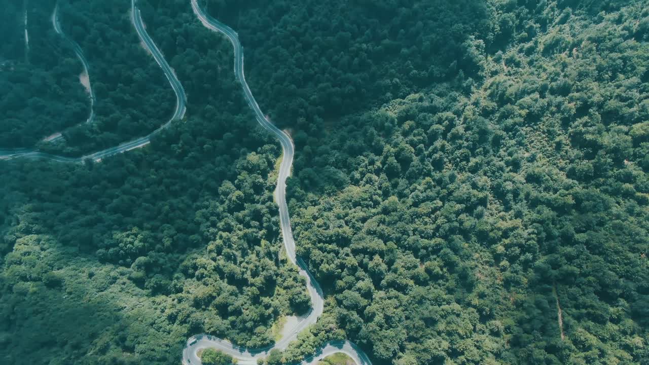 Toma aérea en 4K de coches circulando por una carretera con curvas en la ladera de una montaña