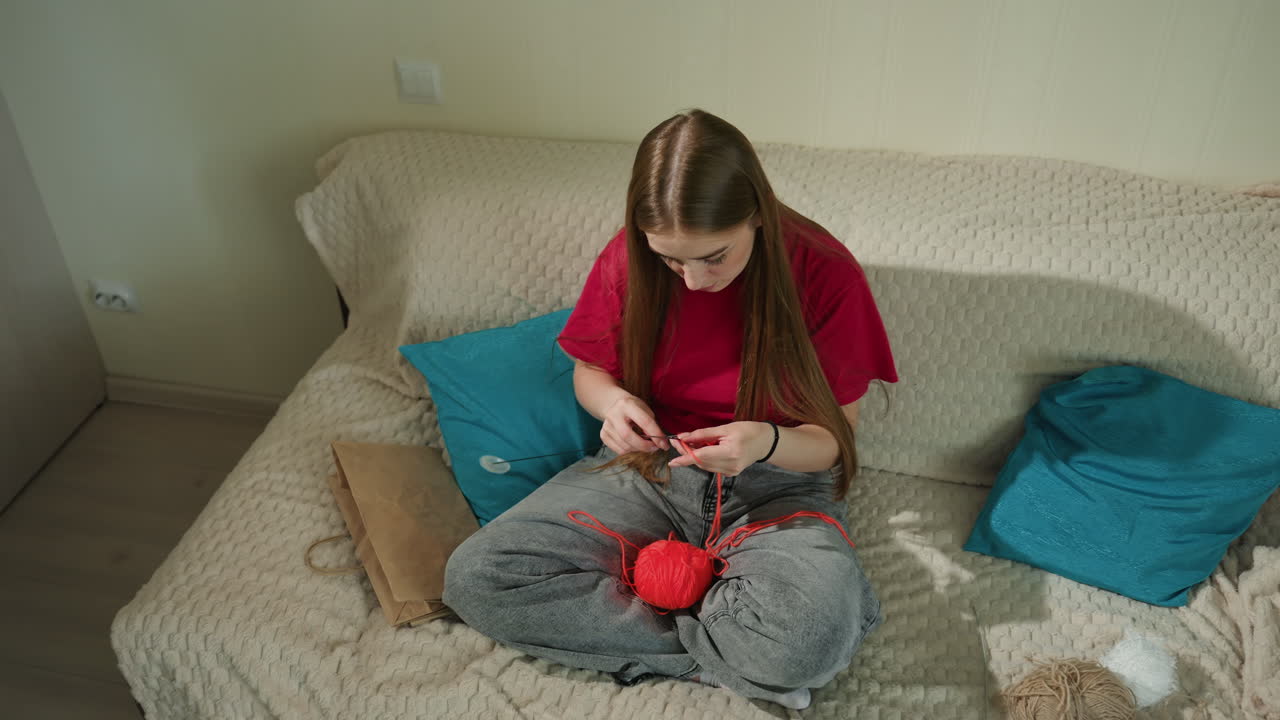 Donna che lavora a maglia comodamente, scena interna di una donna che lavora a maglia nel tempo libero, momento domestico informale di una donna che crea con il filato, ambiente domestico rilassato in cui una donna lavora a un progetto a maglia con attenzione