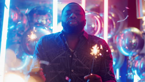 joyful african man having fun at party. guy holding sparkles on neon background