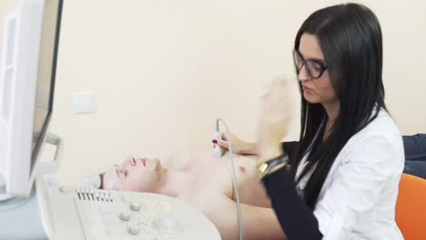 Young-female-doctor-in-glasses-is-screaning-her-patient's-heart-with-ultrasonography,-looking-at-the-screen.-Healthcare-concept