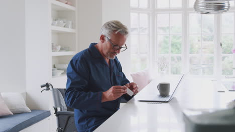 Älterer-Mann-Im-Rollstuhl-Zu-Hause-Sucht-Online-Mit-Laptop-Nach-Informationen-über-Medikamente