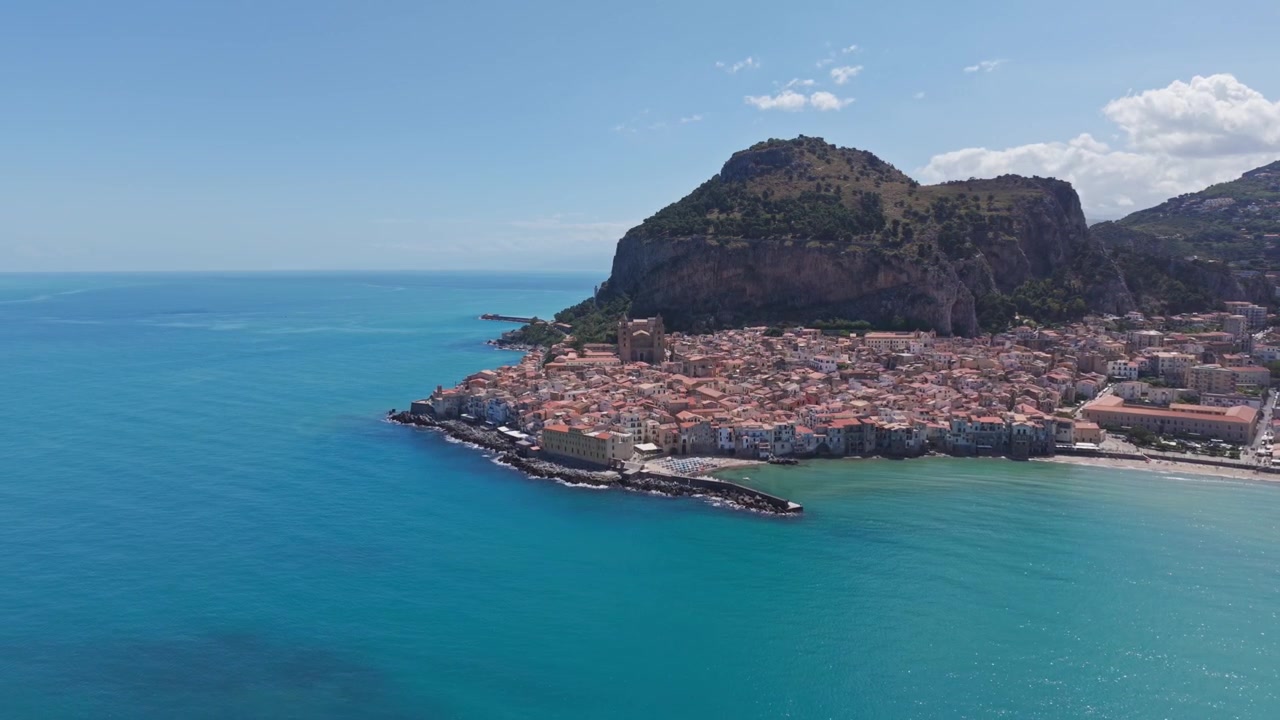 Veduta aerea di una cittadina costiera con mare turchese e paesaggio montano