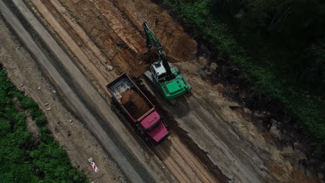 Top-down-aerial-view-of-truck-and-bulldozer-loading-and-unloading-soil-at-the-road-construction-site