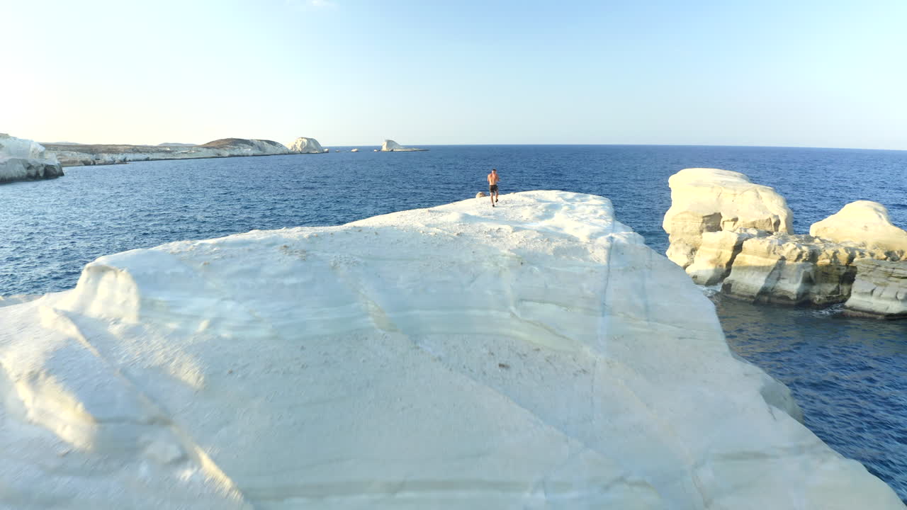 Filmato aereo cinematografico fluido con drone della spiaggia di Sarakiniko con una persona nell'isola di Milos, Grecia, al tramonto in 4K.