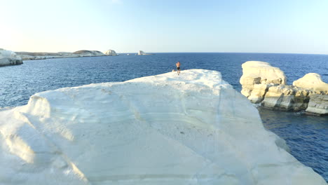 smooth cinematic aerial drone footage of sarakiniko beach with a person in milos island, greece at sunset in 4k