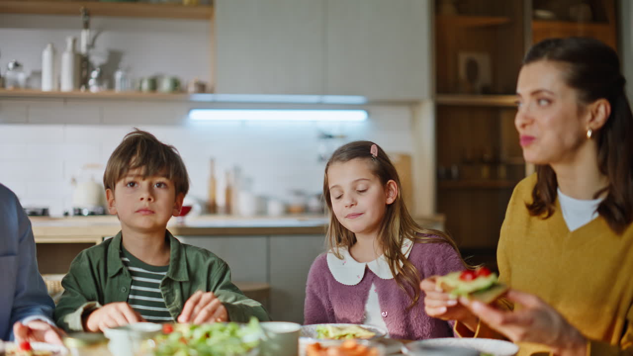Genitori e figli pranzano insieme in cucina, primo piano. Persone che masticano panini