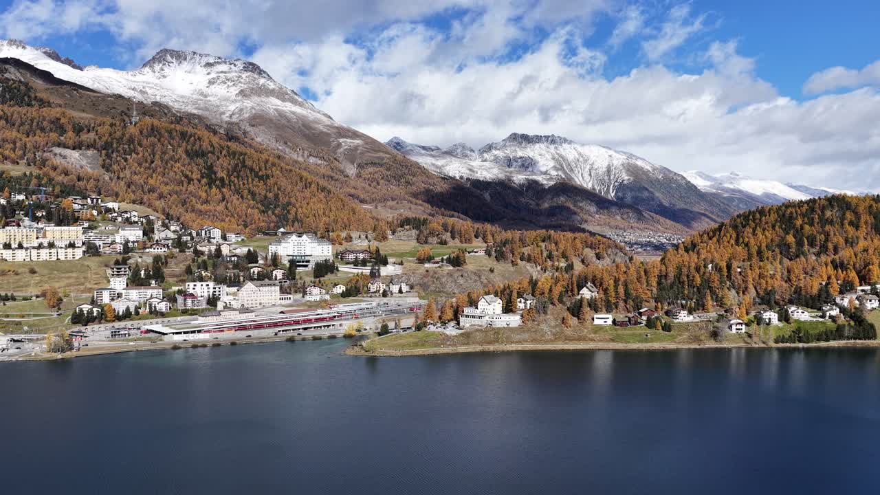 Sankt Moritz lake surrounded by golden autumn forest and snowy alps in Engadin Switzerland, peaceful mountain landscape with blue water and clear sky