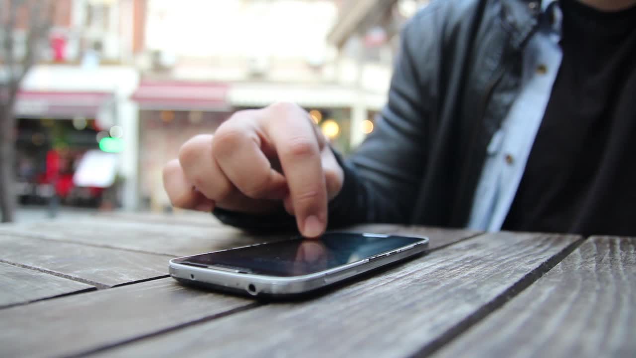 카페에서 스마트폰을 사용하는 젊은 남자가 손을  ⁇ 고 있습니다.