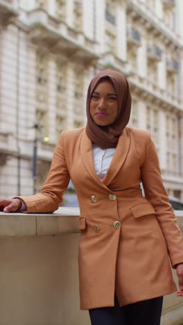 Vertical-Video-Portrait-Of-Smiling-Muslim-Businesswoman-Wearing-Hijab-And-Modern-Business-Suit-Standing-Outside-City-Office-Buildings-1