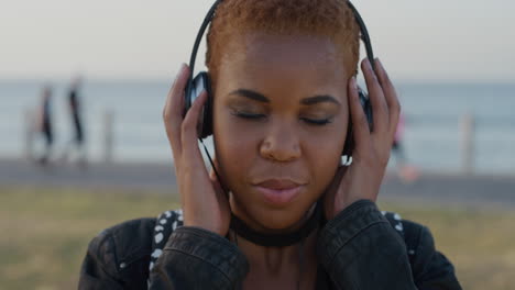 portrait young african american woman puts on headphones listening to calm music enjoying relaxation on beautiful summer seaside day slow motion