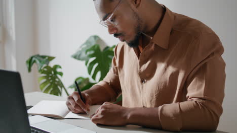 focused freelancer writing notes in office. dreadlocks guy studying attentively