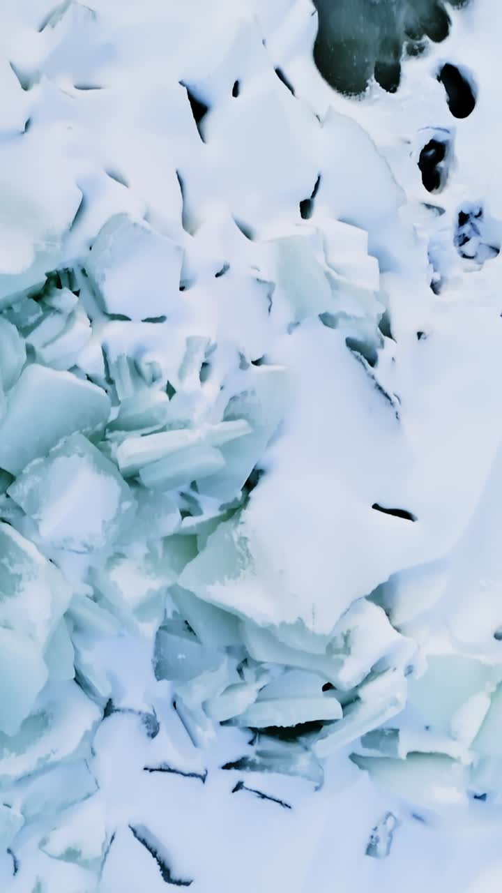 Ripresa verticale dall'alto con drone di ghiaccio marino fratturato, chiazze di schiuma di neve e pozze di acqua di disgelo verde scuro che creano un motivo a trama artica astratto