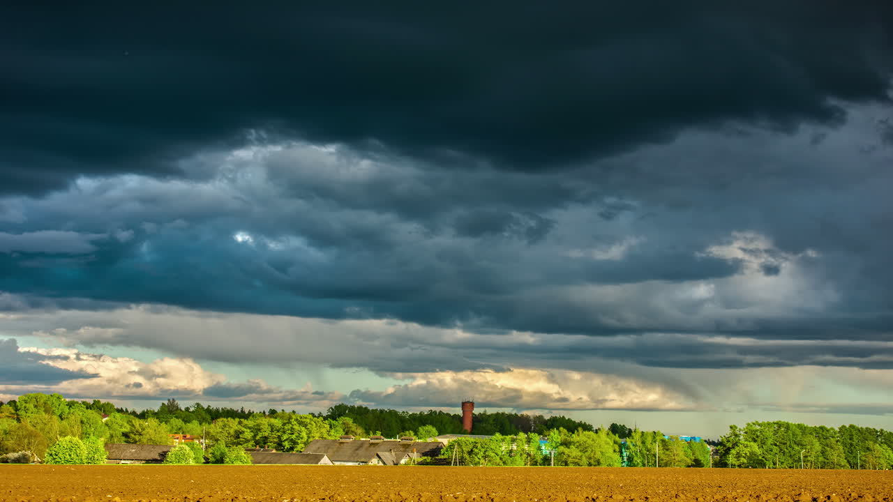 Dark, stormy clouds blowing across the sky above a farmland field or freshly planted crops - dramatic cloudscape time lapse
