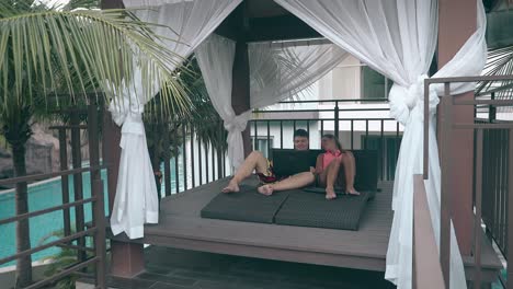 pareja con dispositivos descansa en la terraza de madera del hotel en la piscina