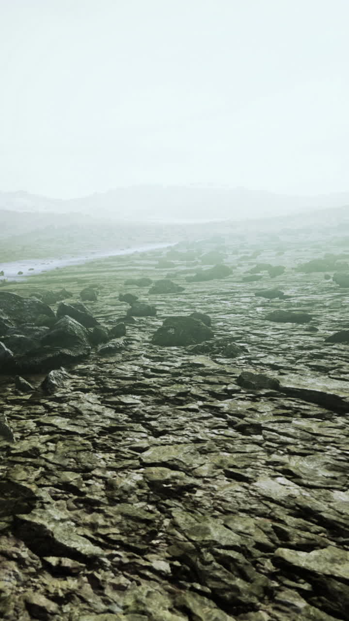 Rocky landscape with river and hills in the distance under foggy sky