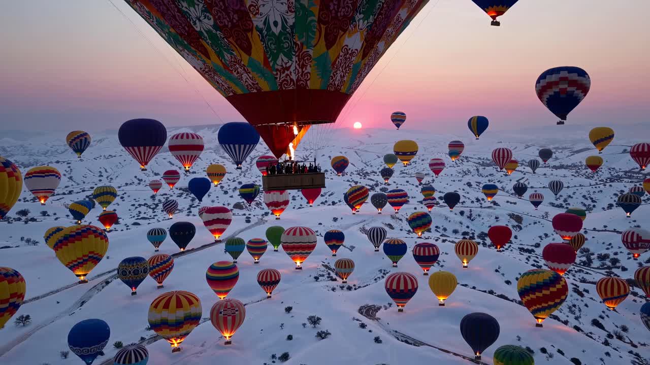 Aerial video captures vibrant hot air balloons floating over snowy landscapes at sunrise