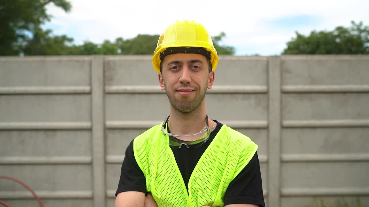 un trabajador de la construcción, vestido con un sombrero amarillo, cruza los brazos sobre su pecho, expresando satisfacción con el trabajo terminado - medio de primer plano