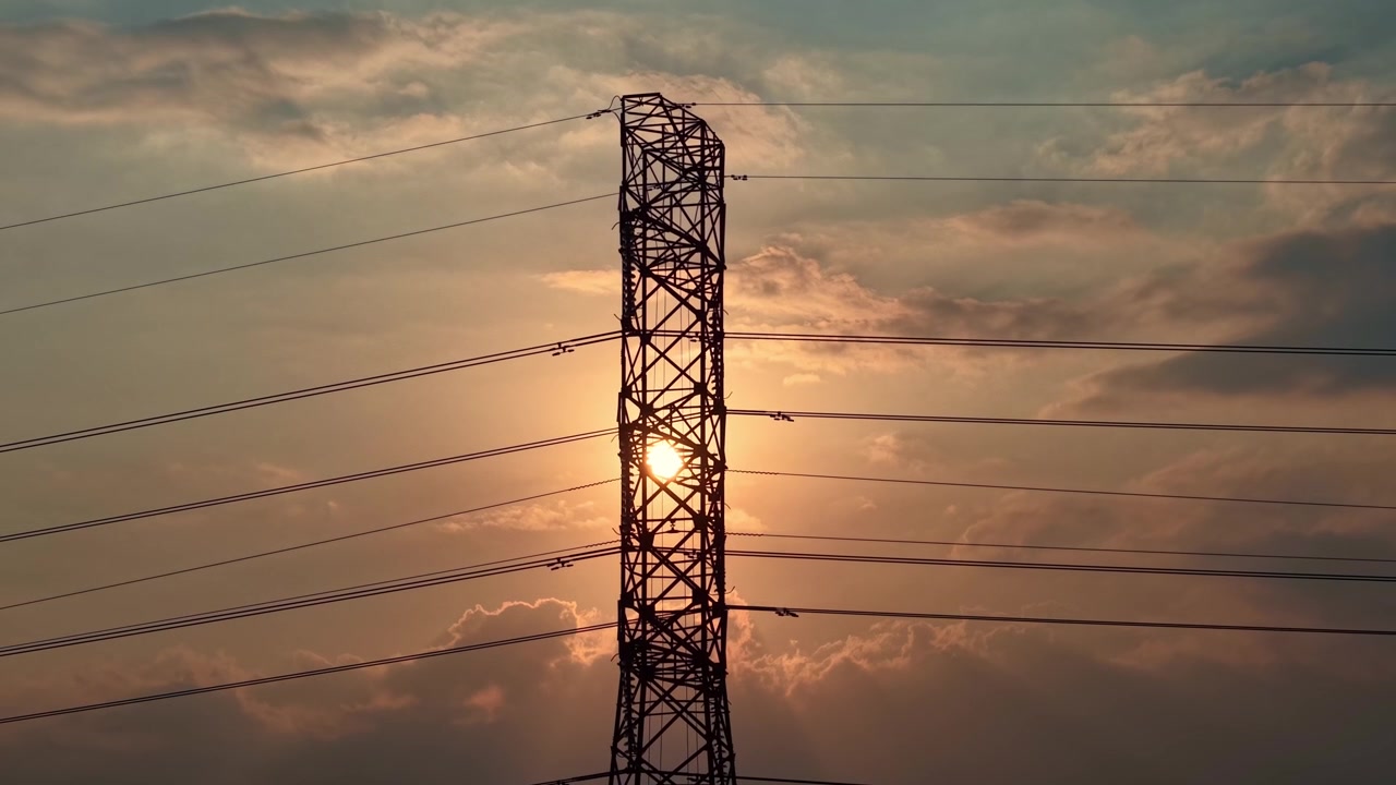 Aerial drone view of Transmission tower silhouette against orange sunset sky, power grid infrastructure, electricity energy concept footage scene.