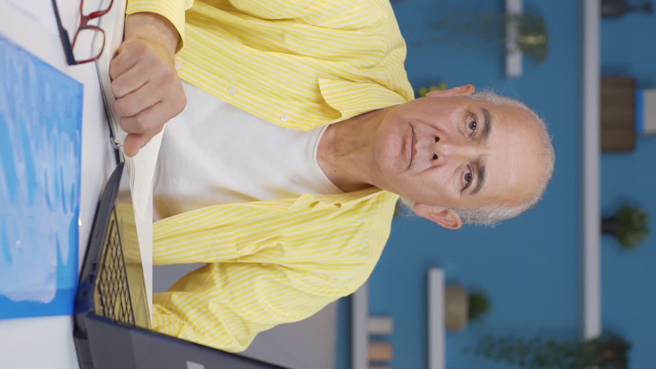 Vertical video of Home office worker old man looking dull at camera.