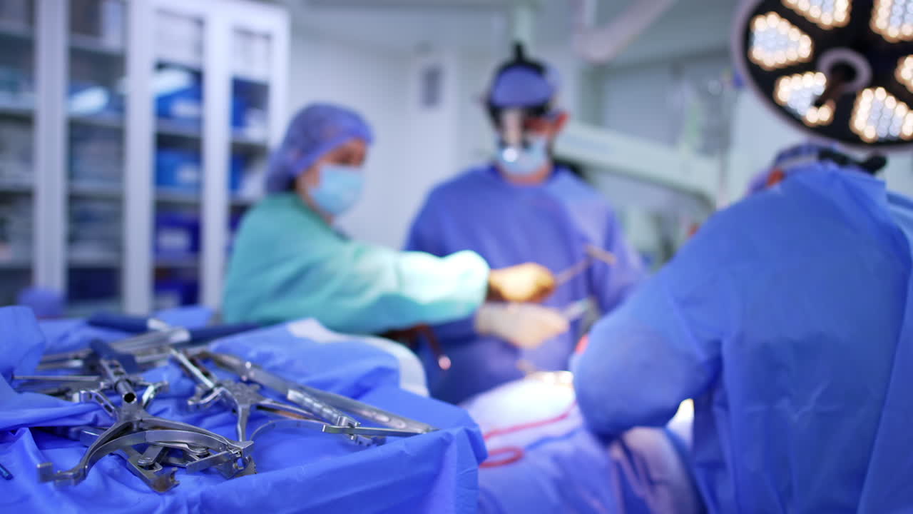 Surgical instruments prepared for neurosurgery. Close up of stainless steel surgical tools lying on sterile table. Neurosurgical team works in background with patient