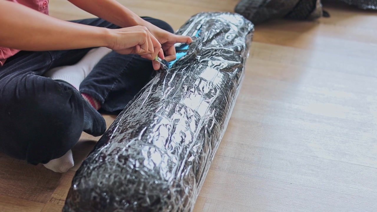 Close-up on hands slicing open plastic bubble wrap packaging with knife while sitting at home