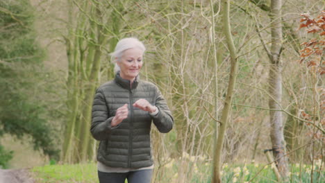 senior woman running in countryside exercising checking smart watch fitness activity app