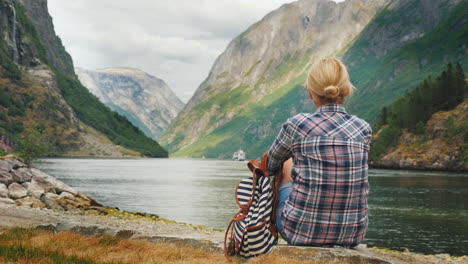 A-Woman-Sits-On-The-Shore-Of-A-Picturesque-Fjord-In-Norway-Admires-The-Beautiful-View-Of-The-Neroy-F