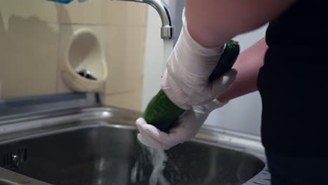 un concombre est lavé sous l'eau courante avec des gants jetables