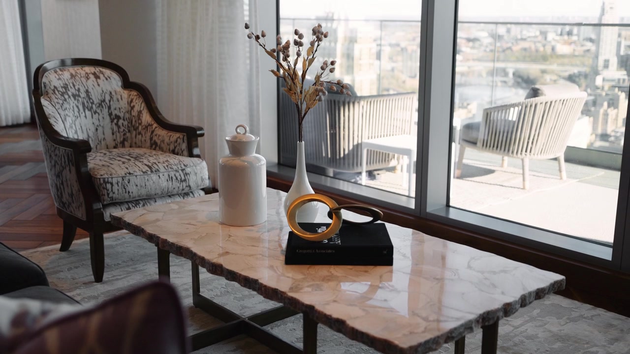 Elegant living room setup with a marble coffee table, decorative vases, and a cozy accent chair, complemented by large windows offering a city view