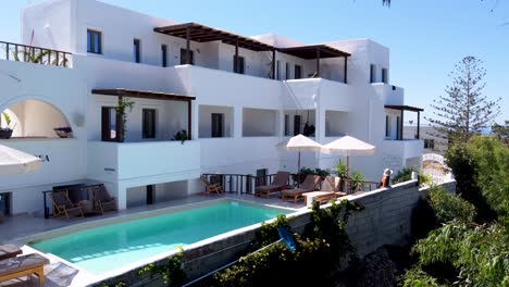 tracking aerial of charming walking woman contemplating typical touristic accomodation terrace, in parea paros hotel