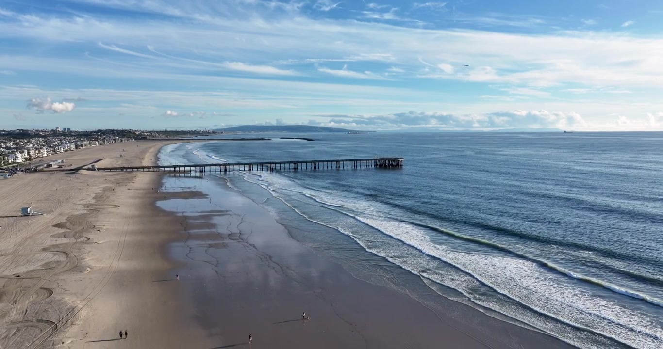 Una ripresa aerea cinematografica grandangolare con drone del Molo di Santa Monica, che si allontana lentamente sopra la spiaggia di Venice e la costa del Pacifico a Los Angeles, California