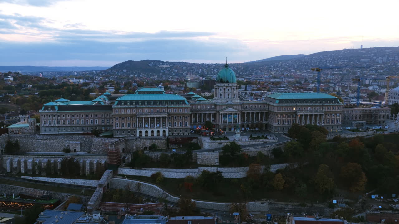 The grand Buda Castle dominates the skyline as it rests majestically atop Castle Hill, framed by autumn colors and evening light