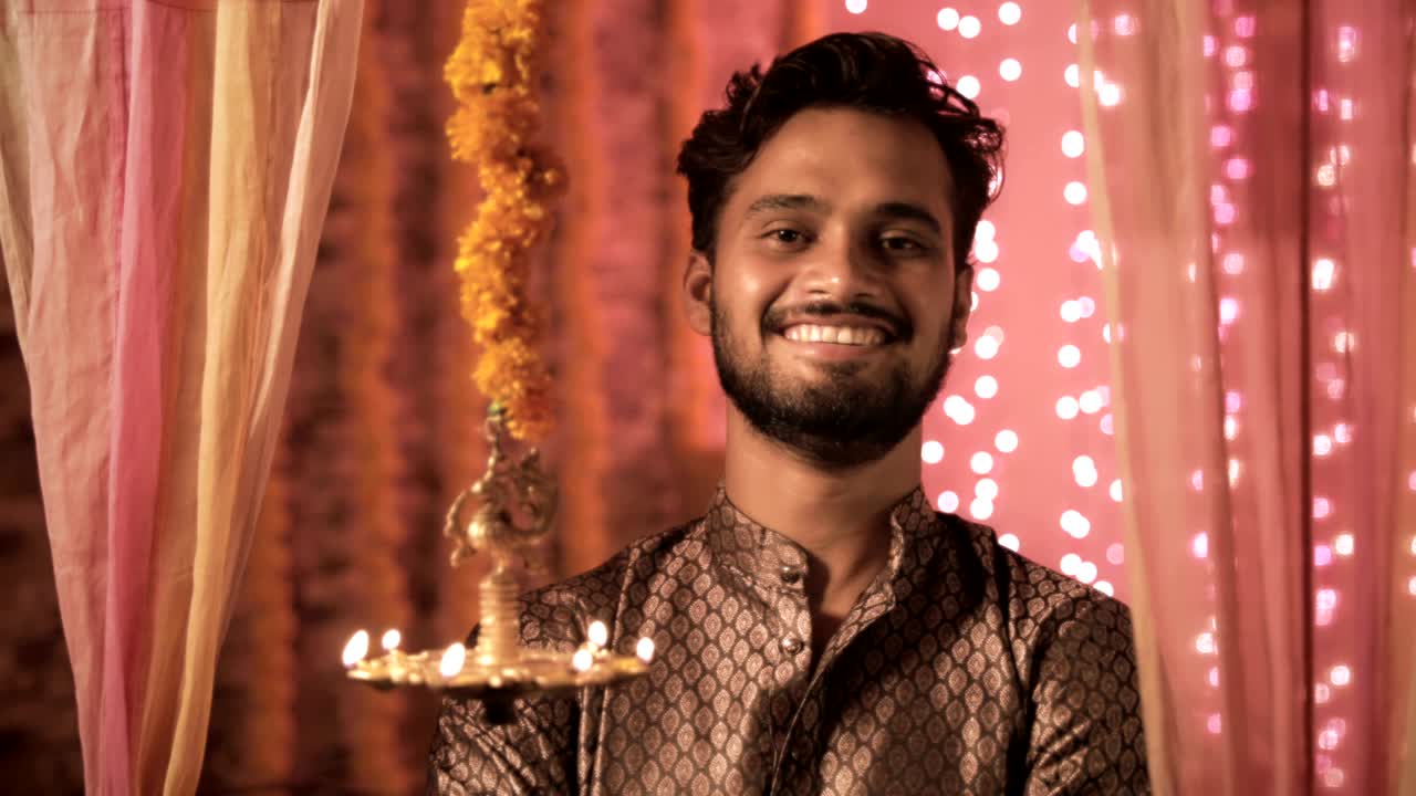 Un giovane felice che sorride davanti alla lampada a olio appesa, in abiti tradizionali, durante il festival di Diwali.