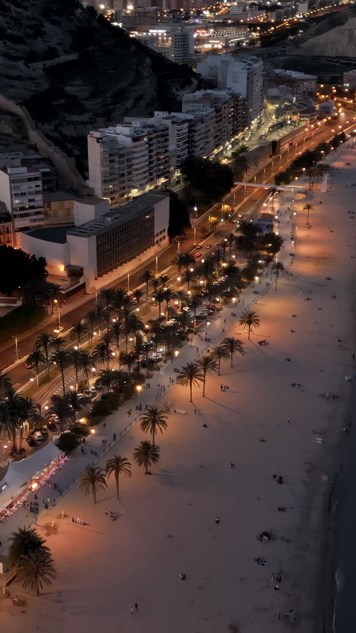 Aerial drone view of cars moving along the coastline in Alicante, Spain in the evening. Vertical