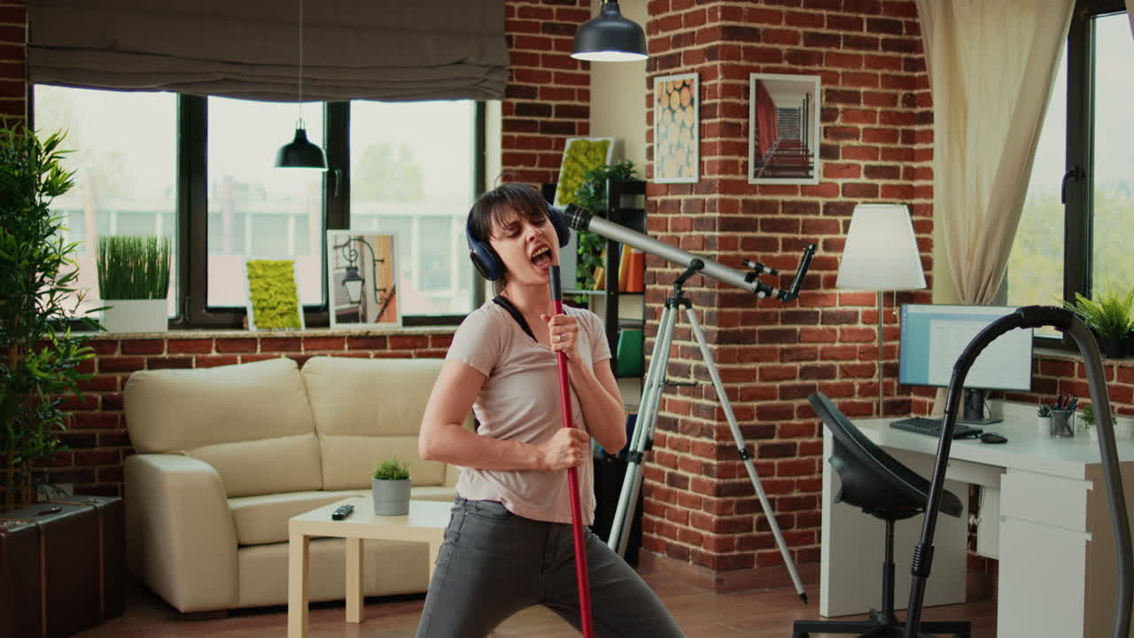 Positive woman listening to music on headphones and vacuuming apartment floors