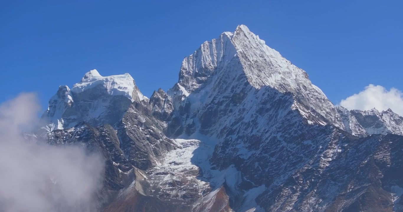 Everest-regionen Nepal, filmisk teleoptagelse af tykke hvide skyer, der bevæger sig hen over Ama Dablam-bjergets barske, sneklædte flade mod en klar blå himmel.