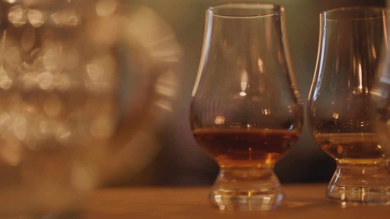 Hand selecting whisky glass from wooden table in cozy, softly lit bar with blurred lights