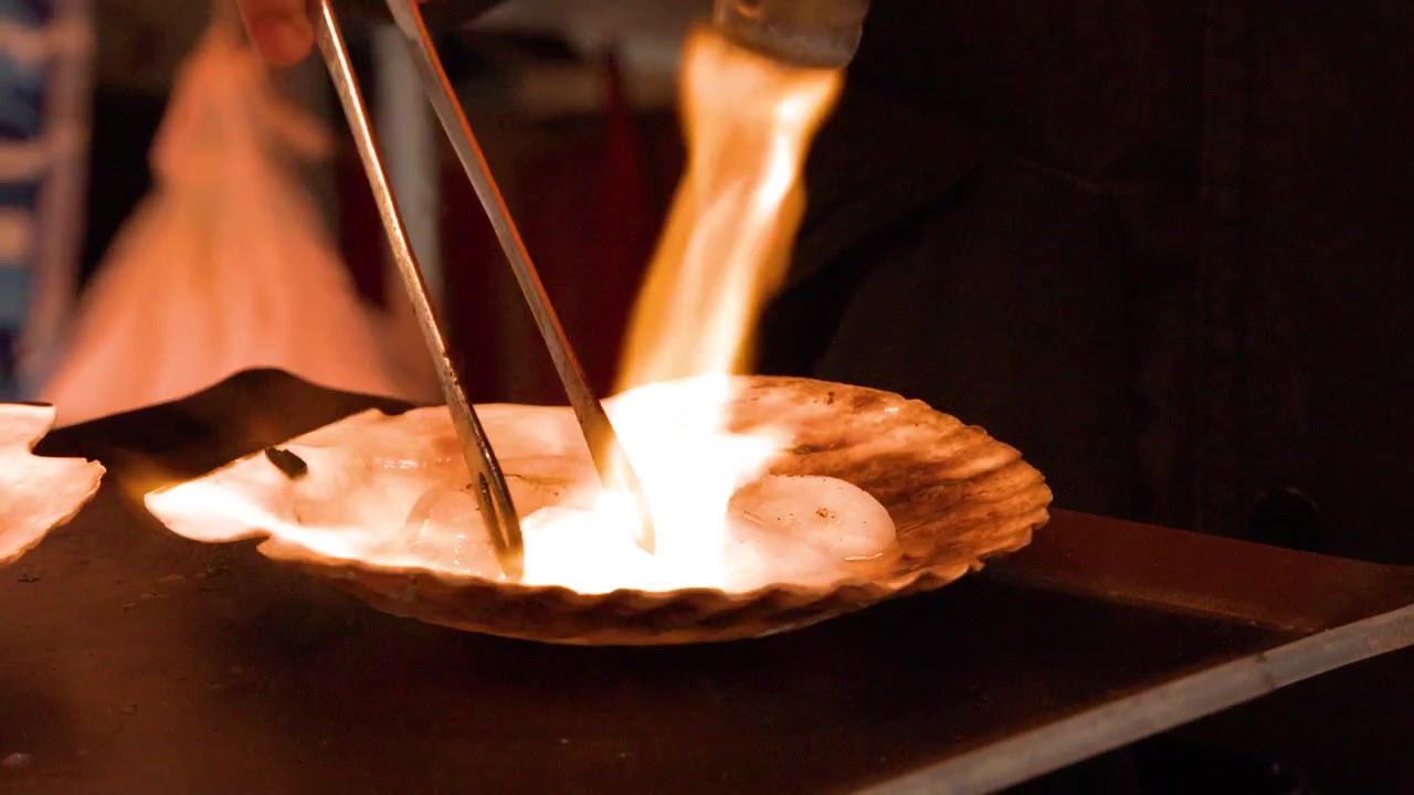 Close-up shot of a street food vendor searing fresh scallops with a powerful blowtorch flame