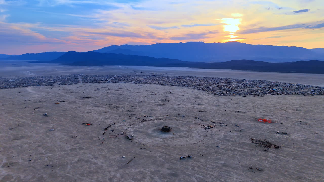 Aerial view of central desert festival ring. A wide aerial shows the circular center and camps stretching toward mountains at sunset
