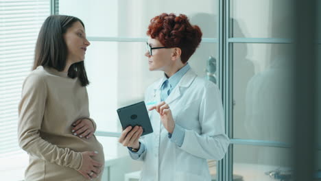 doctor using tablet and consulting pregnant woman in clinic