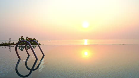 sun reflecting over infinity pool water at sunset with sea in background