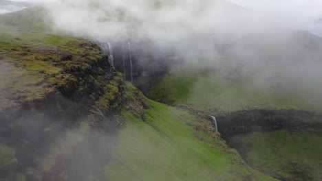 Fossá-Waterfall,-coastal-falls-in-Faroe-Islands-through-misty-clouds,-aerial-pan