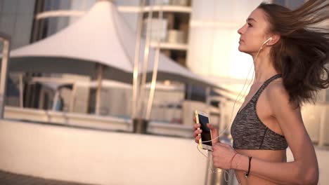 Mujer-Joven-Corriendo-Al-Aire-Libre.-Chica-Fitness-Femenina-Entrenando-Para-Correr-Afuera-Junto-Al-Agua-Escuchando-Música-Con-Auriculares.-Hermosa-Joven-Rubia-En-Sujetador-Deportivo.-Vista-Lateral