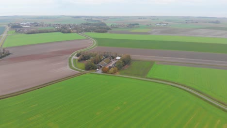 disparo de un dron alto sobre la hierba verde, marrón, tierras de cultivo terrosas y granjas de los países bajos